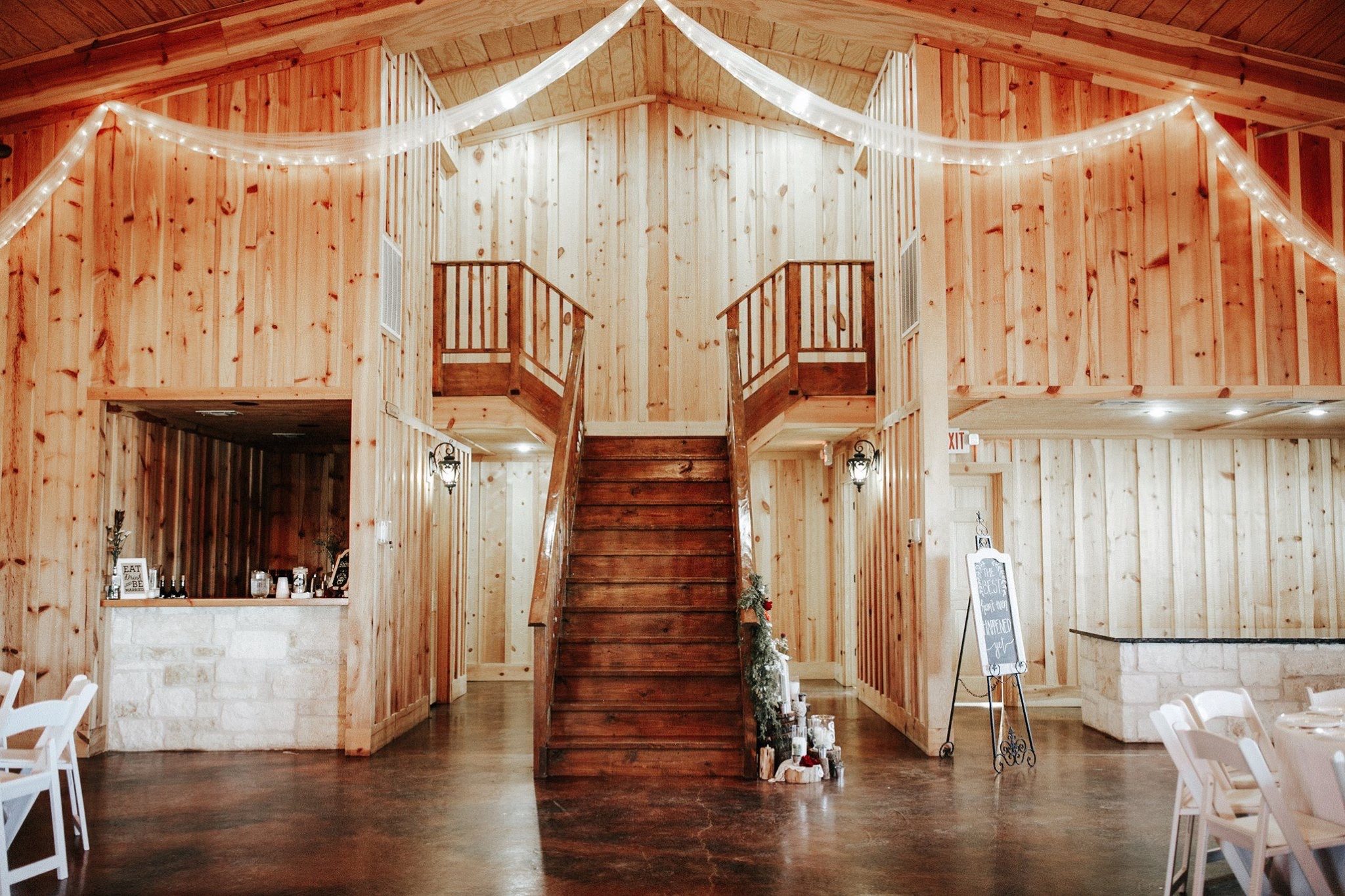 Timber-lined indoor event hall with staircase and draped lights